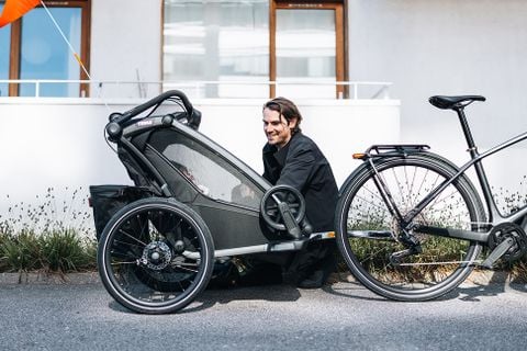 一名男子蹲在一輛附有兒童腳踏車拖車的自行車旁。