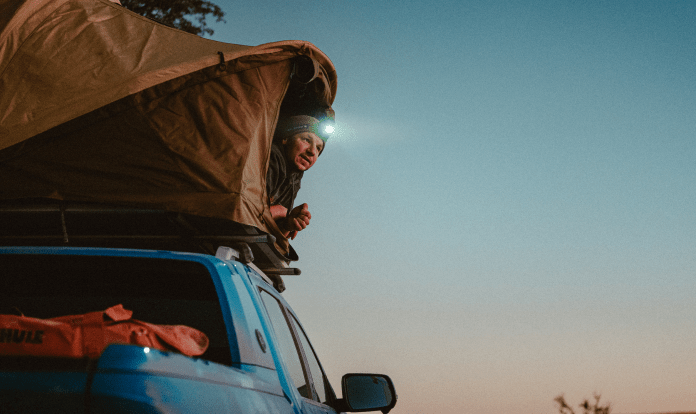 Tobias Woggon looks out of a rooftop tent while wearing a headlamp. 
