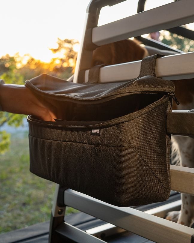 Hand placing an item into a storage bag attached to a Thule Allax dog crate.