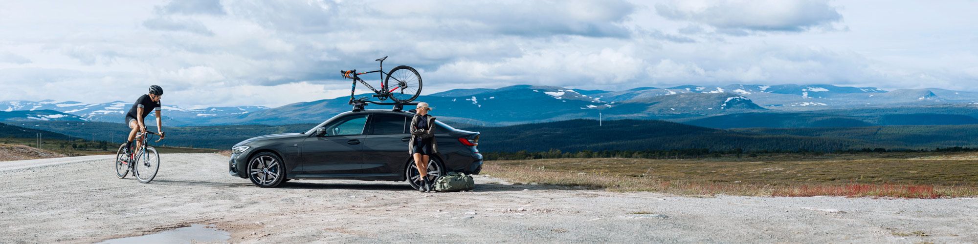 On a mountainous country road two cyclists have brought their bikes on a Thule roof bike rack.