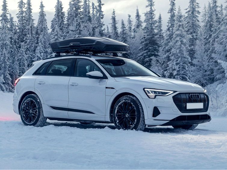 A car drives in a snowy forest with a Thule Motion XT rooftop cargo carrier.