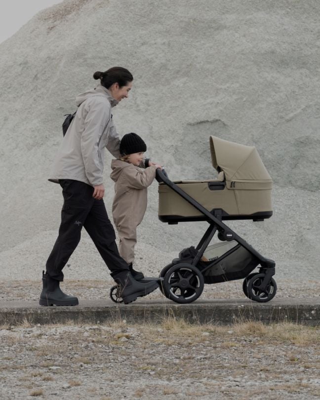 Parent pushing a Thule stroller with a child outdoors.