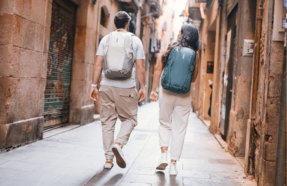 Two people walk down a narrow alleyway in the city carrying Thule Enroute backpacks. 