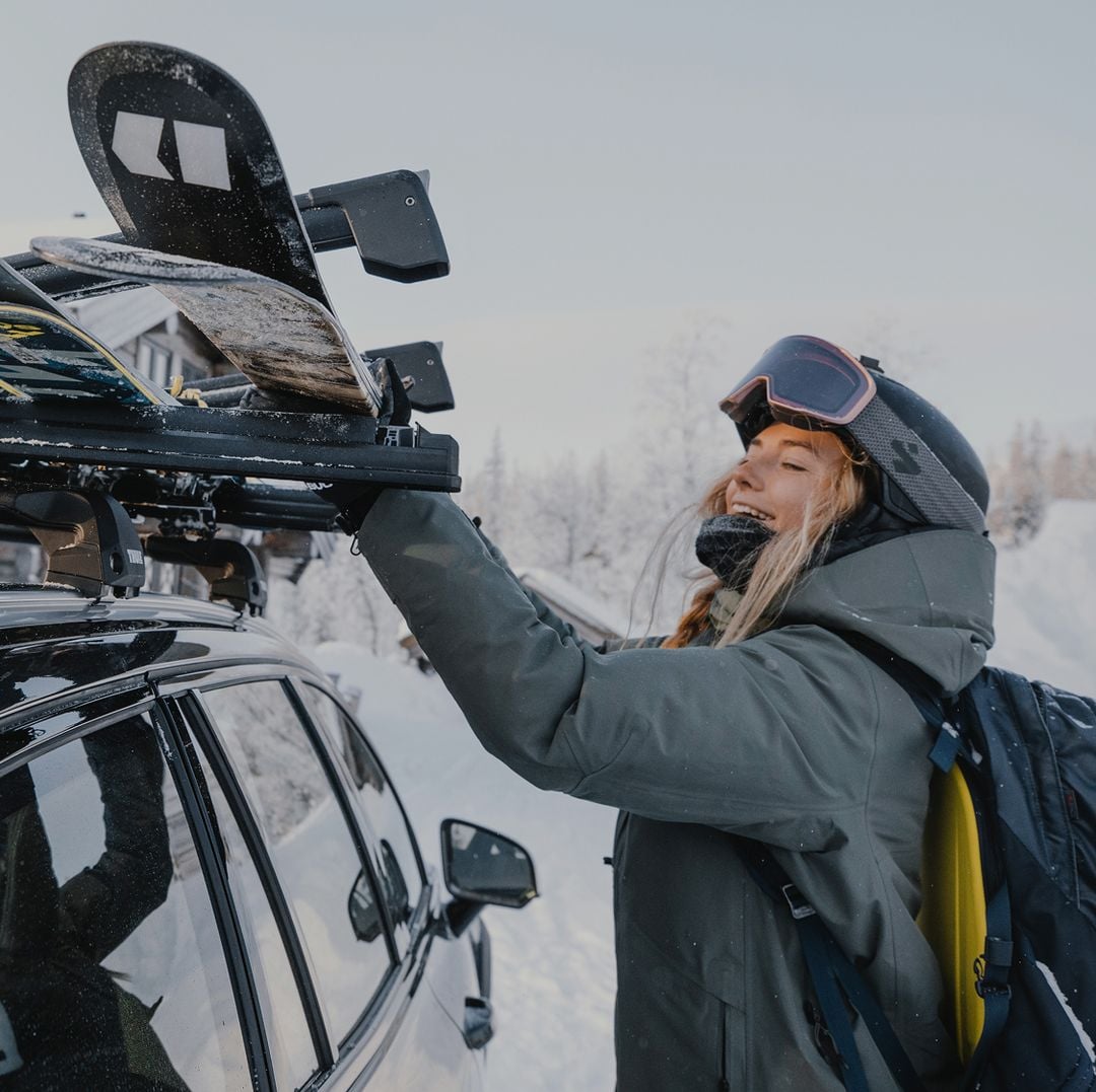 Person loading skis onto a car with Thule ski racks in a snowy mountain setting.