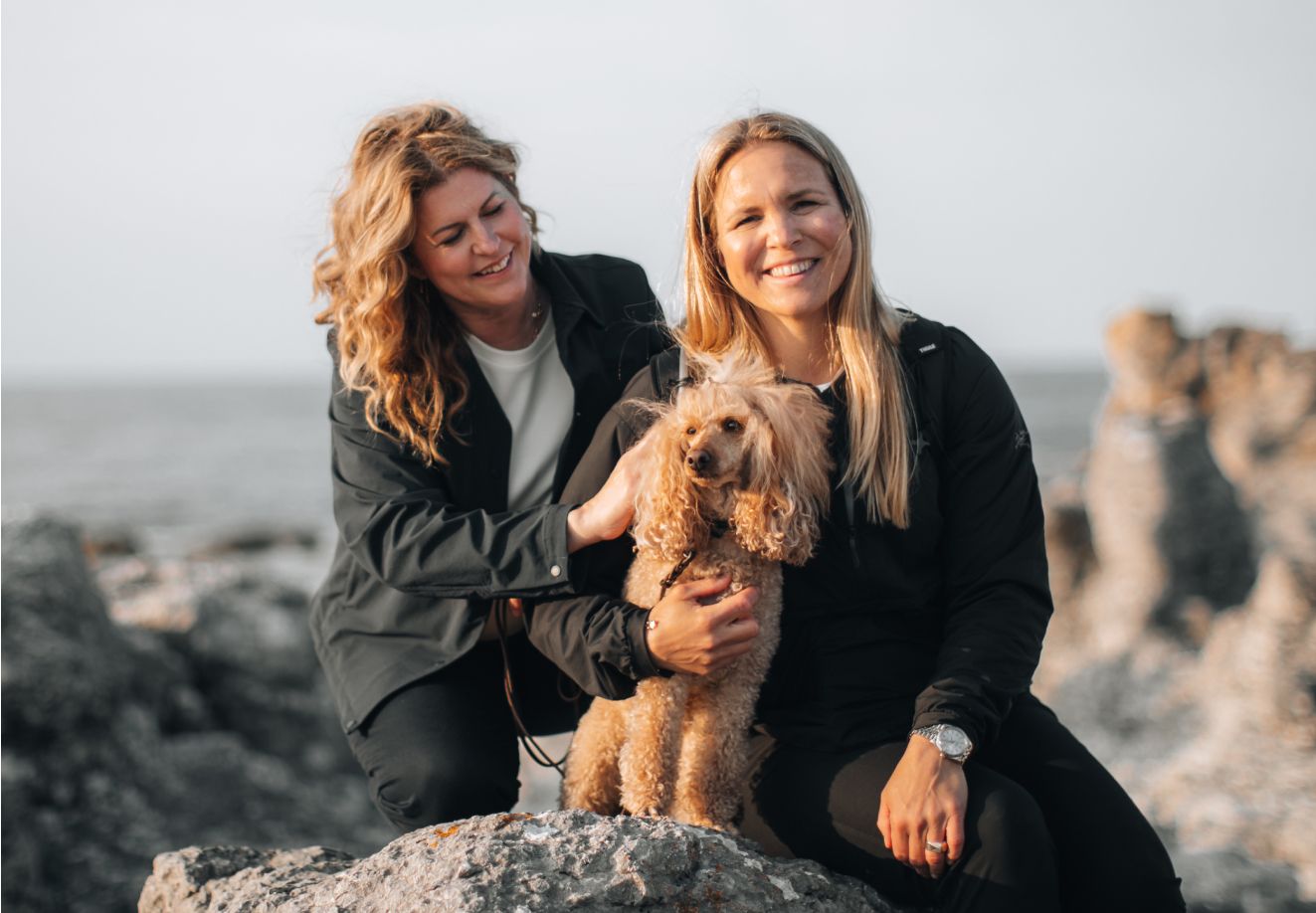 Anja Pärson a Filippa Rådin pózují se svým psem a usmívají se do kamery.