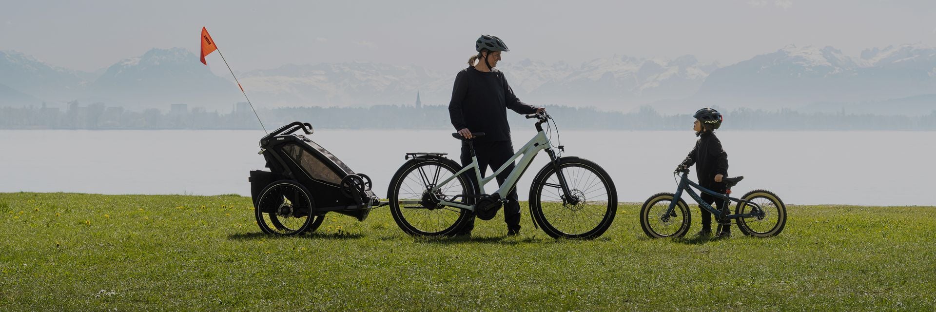 Un parent faisant du vélo avec une caravane d’enfant dans un cadre naturel.