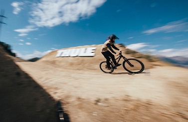 Uma pessoa a andar de bicicleta por um monte de terra com um grande logótipo branco da Thule. 