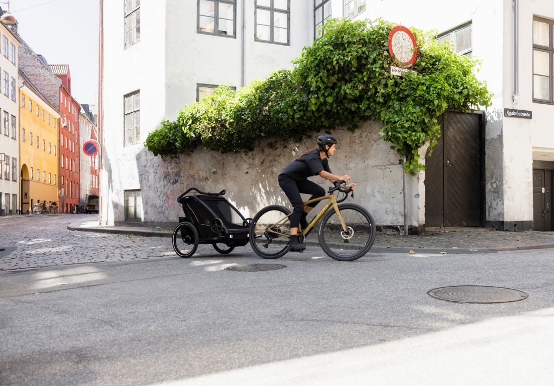 A woman is biking with a Thule Chariot Sport 2 bike trailer in an urban environment