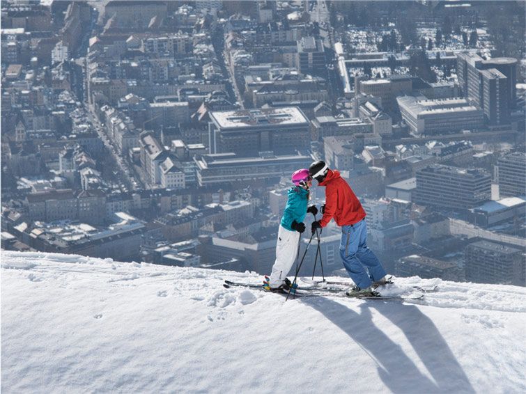 Two skiers ski at the snowy mountain at Nordkette ski resort that looks over the city of Innsbruck.