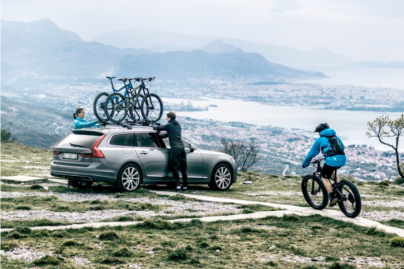 2人のサイクリストが山のそばにある屋根付きの自転車ラックに自転車を積み込み、下の町を見下ろしています。
