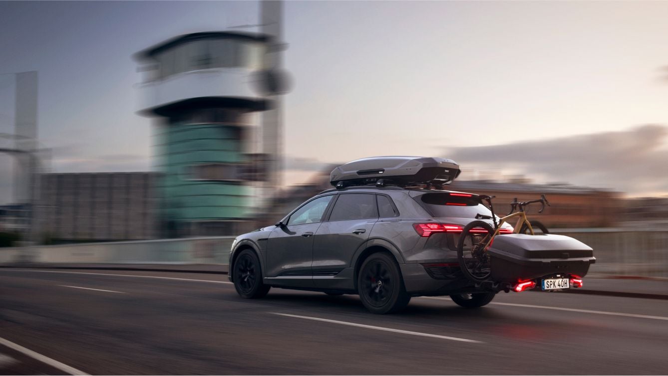 A driving SUV with Thule roof box, rear bike carrier and a cargo carrier mounted on the back of the car.