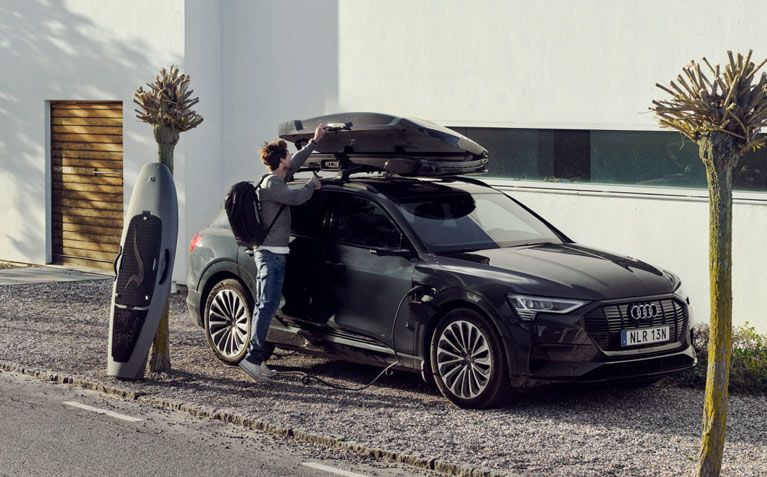 A man loads a Thule roof box while wearing a Thule Chasm backpack