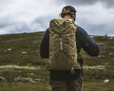 A man walks down a mountain trail carrying a hiking backpack.