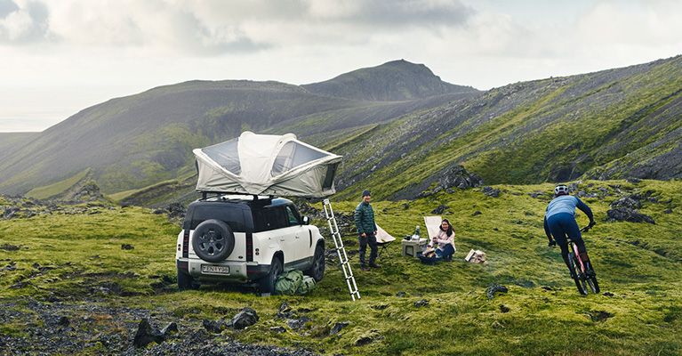 A vehicle in the foggy mountains has a Thule Approach roof top tent and cyclists around it