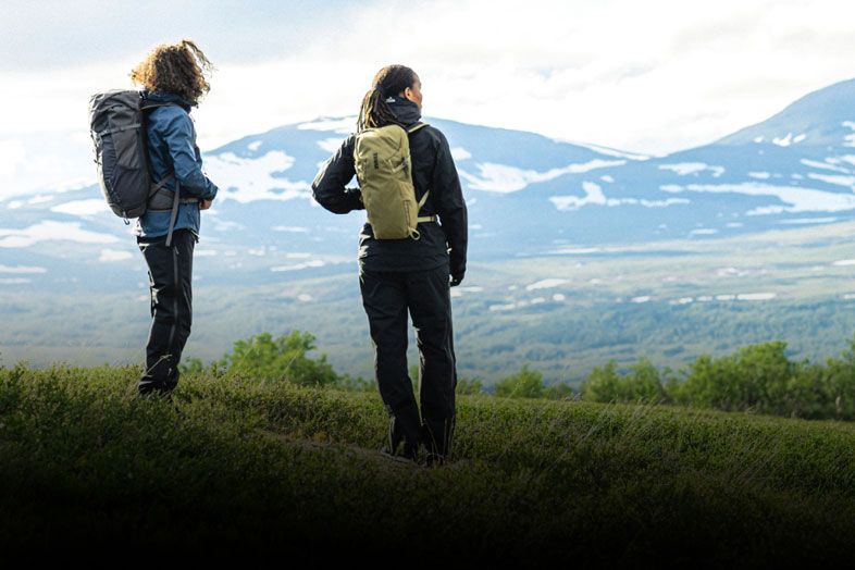 Two hikers look across a hill carrying Thule hiking backpacks.
