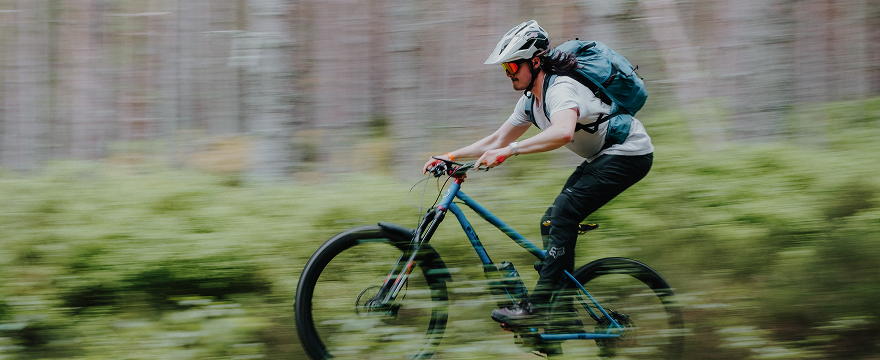 Person riding a mountain bike at speed with a Quad Lock™ through a forest trail, wearing a helmet and backpack.