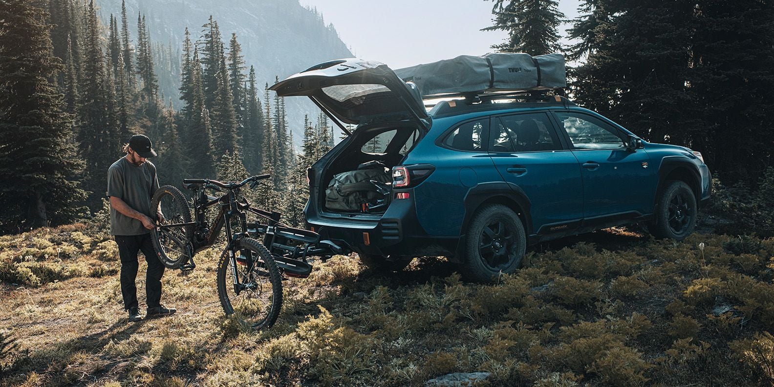 Un uomo utilizza Thule Bike Repair Holder (venduto separatamente) per lavorare sulla sua bici dietro la sua auto