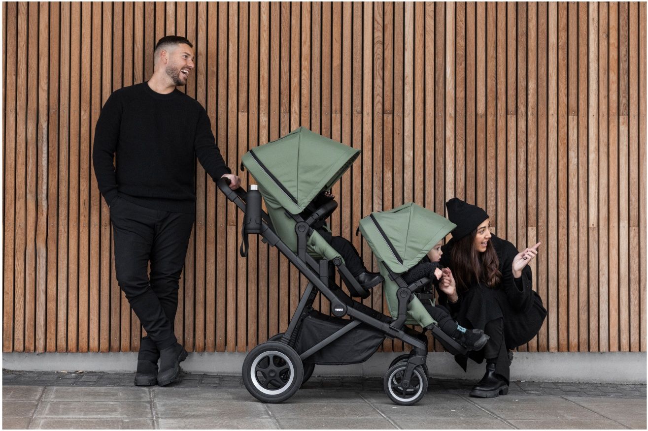 Parents stand next to the best stroller at Thule for two kids in green.