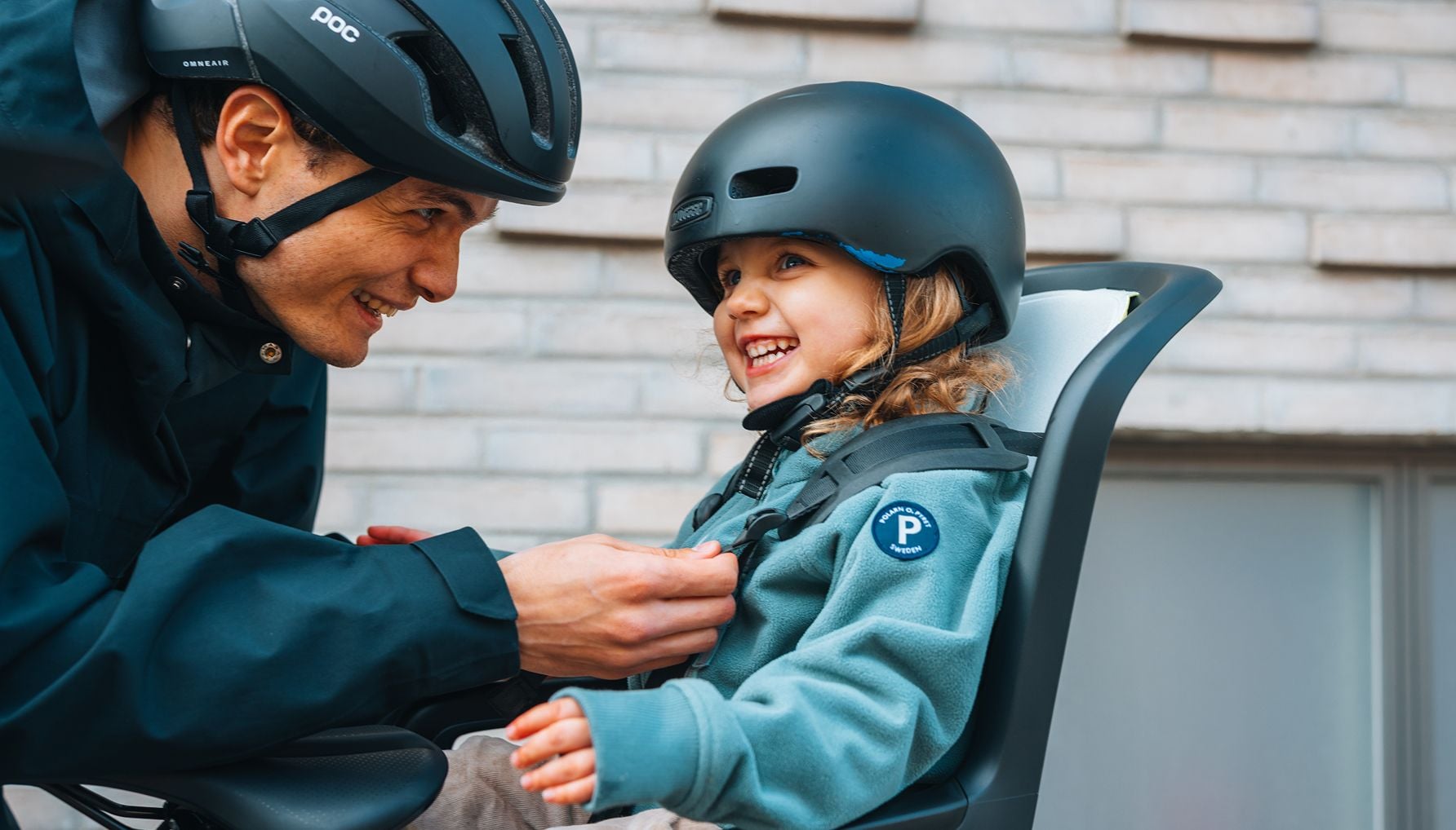Niño con casco sentado en un asiento trasero de la bici, mirando hacia arriba a un adulto.