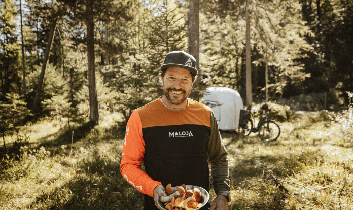 Markus Sämmer stands in the forest and smiles while holding a place full of wild mushrooms.