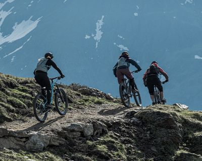 Drie fietsers met Thule Vital drinkrugzakken fietsen over een bergpad.