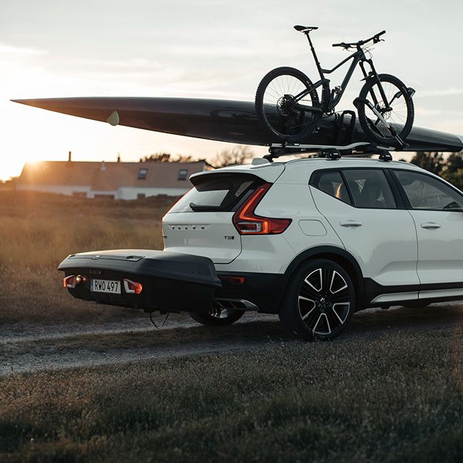 Un SUV blanc avec un v&#xE9;lo et un kayak sur le toit, un coffre sur boule d&#x27;attelage &#xE0; l&#x27;arri&#xE8;re.