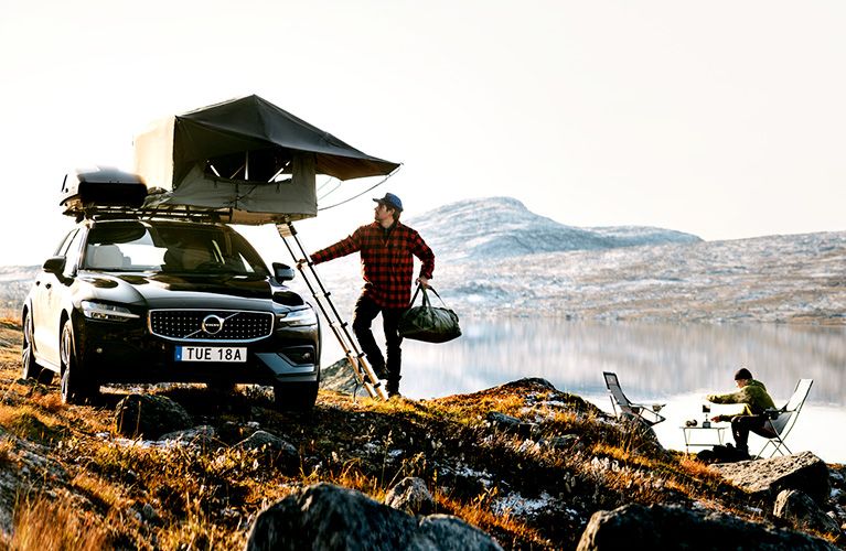 Two people have their vehicle parked in a field by a river with a Thule roof rack, roof box and rooftop tent.