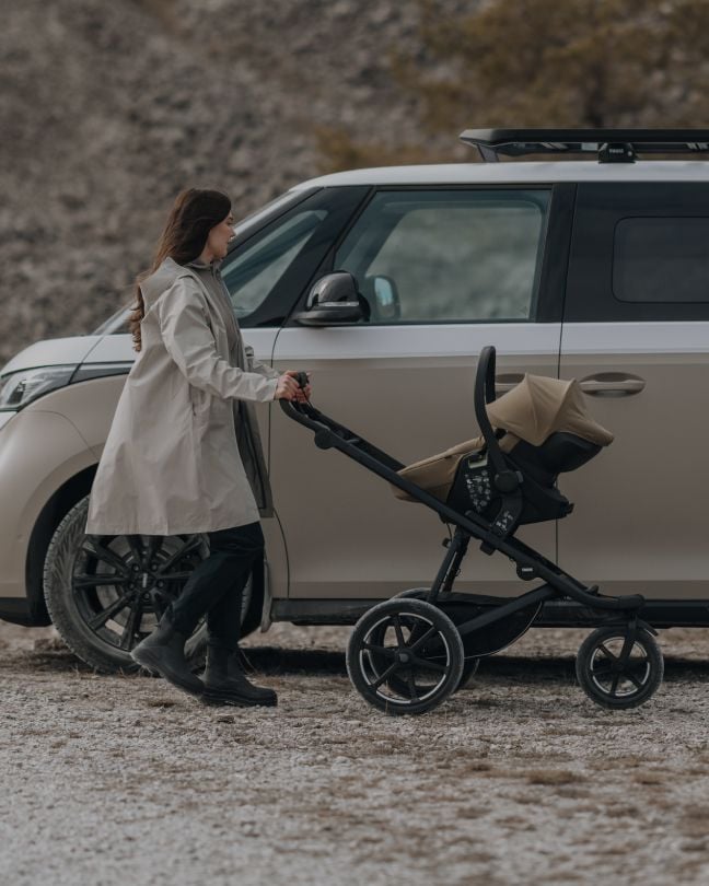 Parent loading a child into a Thule stroller beside a car.