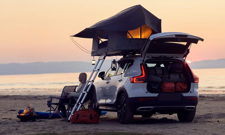 Woman sits underneath a Thule Tepui Foothill roof top tent with a camp fire by the ocean.