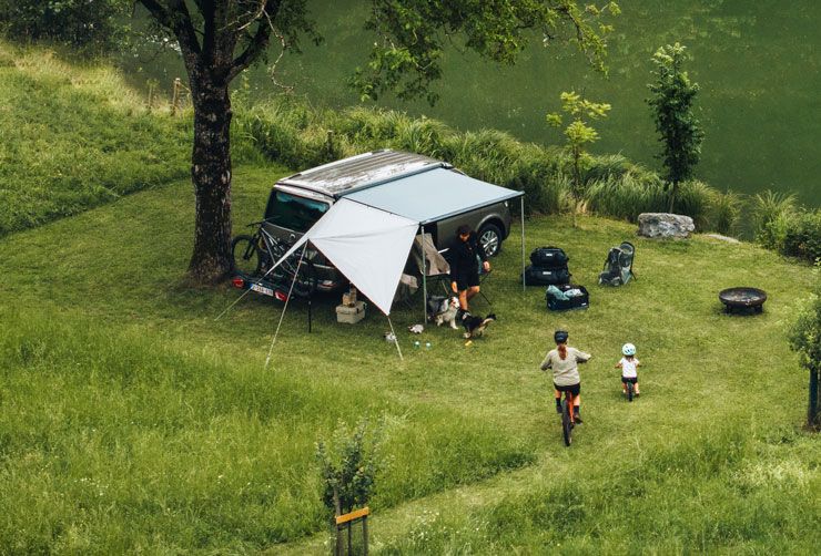 A bird’s eye view of a compact van with the Thule Subsola panels parked in the grass next to a lake.