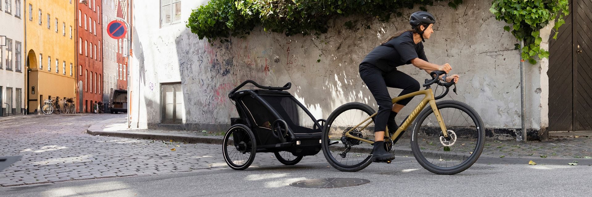 A woman rides a bike down a city street while towing a Thule bike trailer.