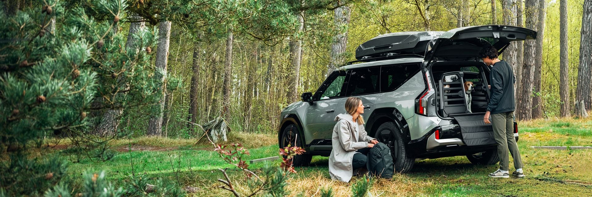 Duas pessoas descarregando equipamentos de um SUV com uma caixa de carga no teto em uma floresta.
