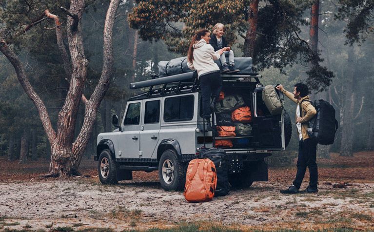 In a misty forest a family unloads Thule Chasm bags from their jeep which has a Thule rooftop tent on the roof.