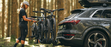 Person, die Mountainbikes an einem Thule-Fahrradträger befestigt, der an einem Auto im Wald befestigt ist.