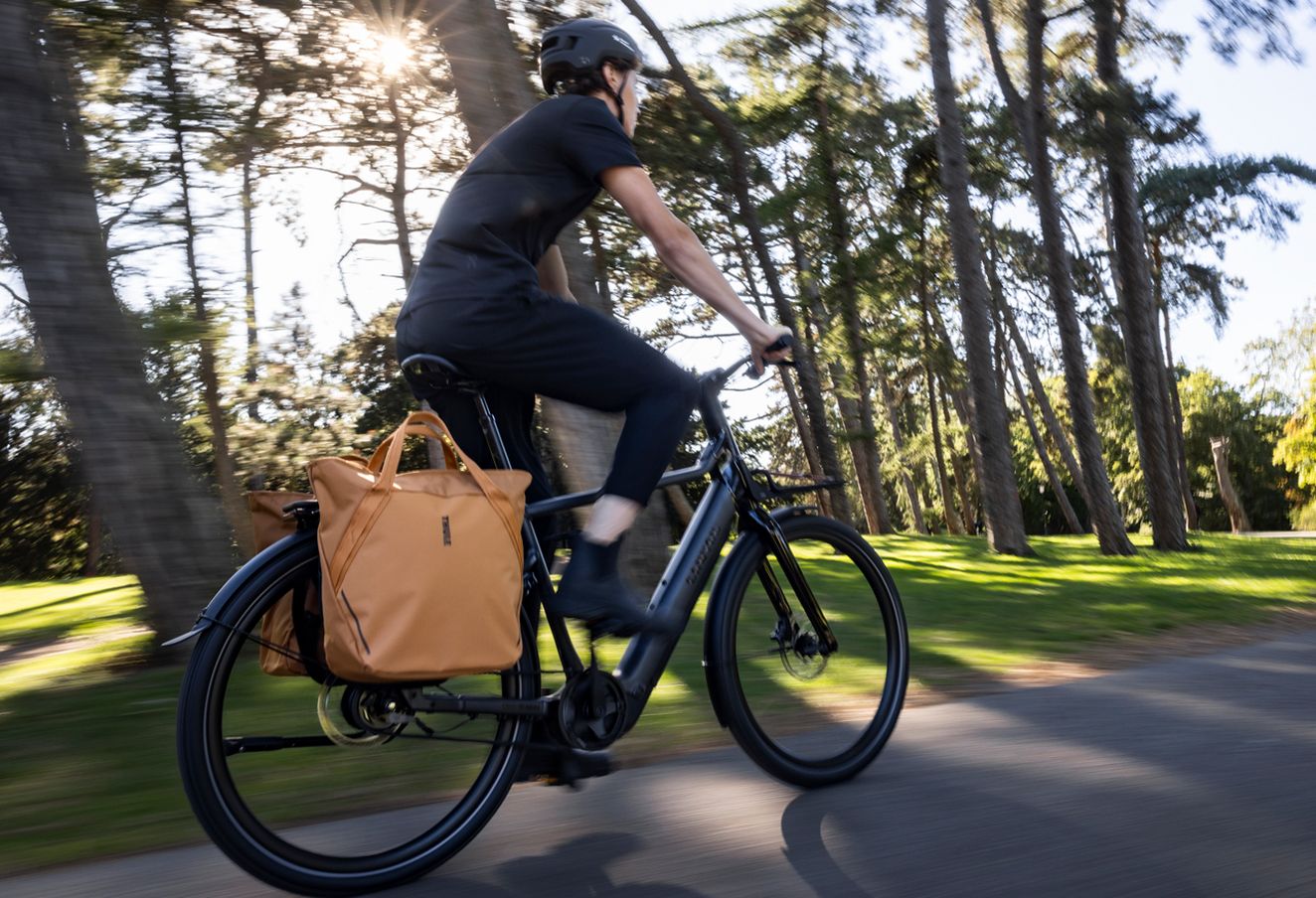 Pessoa a andar de bicicleta com um saco Inlock System by Thule preso ao suporte traseiro.