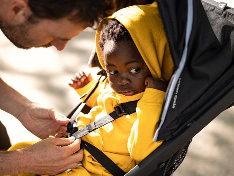 A baby is being strapped in by his father in an terrain stroller.