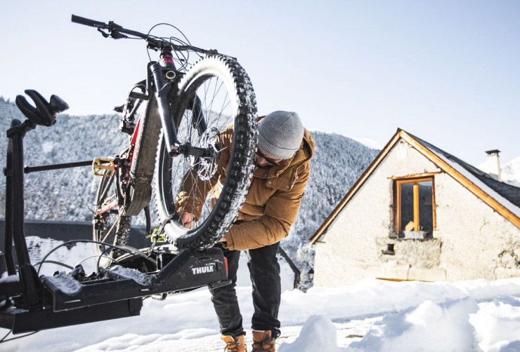 Xavier De Le Rue attaches his winter MTB bike to a Thule bike rack with snowy mountains in the background.