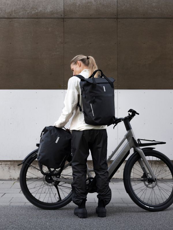Um ciclista está em frente a uma bicicleta elétrica cinza montada no sistema InLock de alforges da Thule, junto com duas bolsas pretas Thule Shield.