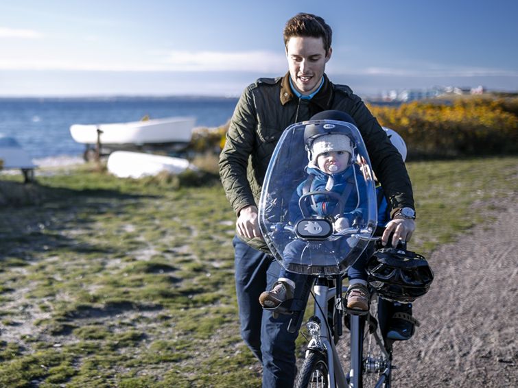 A man walks with his bike by the ocean with his baby in one of the Thule front child bike seats.