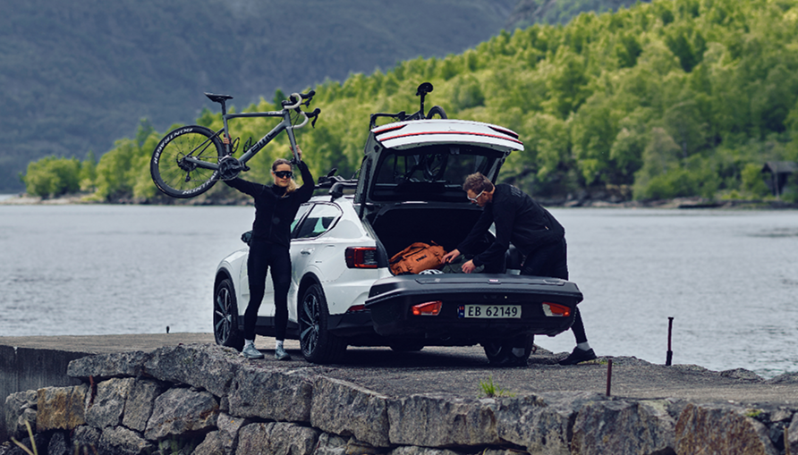 후방에 화물 운반이 장착된 차량. 한 사람은 지붕에서 자전거를 내리고 있고, 다른 한 명은 열린 트렁크에 접근하고 있습니다.