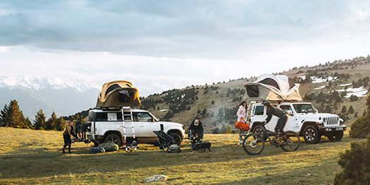 On a mountain a group of friends prepare their camp next to two jeeps with Thule Approach car roof tents on top