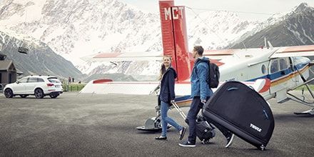 A man and a woman walk next to an airplane by the mountains with their bike travel cases.