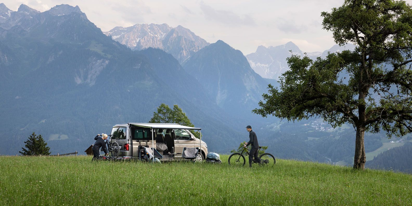 A van is parked in the mountains with the Thule Sidehill awning and a bike carrier.