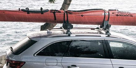A couple with a kayak walk towards a parked car by the water with a kayak on one of the Thule kayak racks.