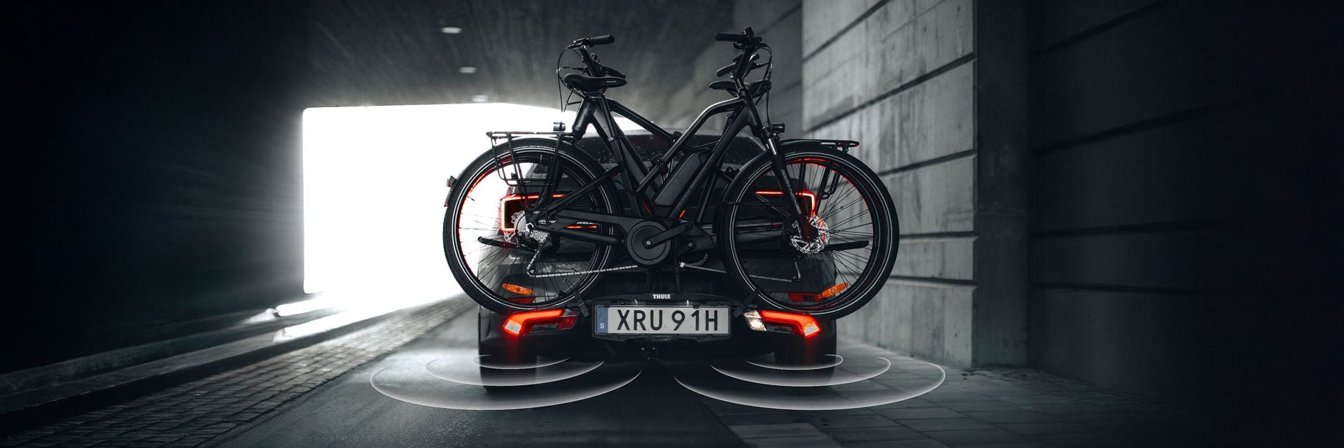 Deux vélos montés sur un porte-vélos Thule Epos à l’arrière d’une voiture traversant un tunnel.