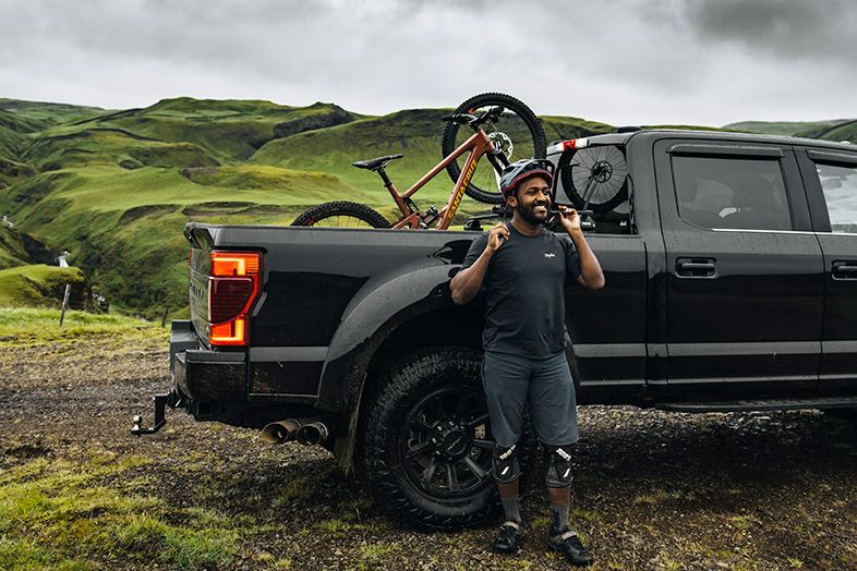 Eliot Jackson securing his helmet with a pickup truck and a Thule truck bike rack with a bike in the back.