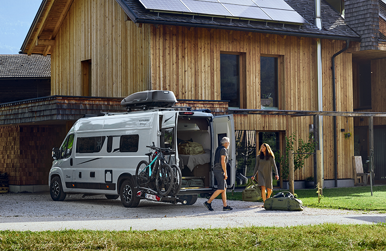 A couple unload gear from their van with e-bikes and a bike rack on the Thule VeloSwing van e-bike carrier.