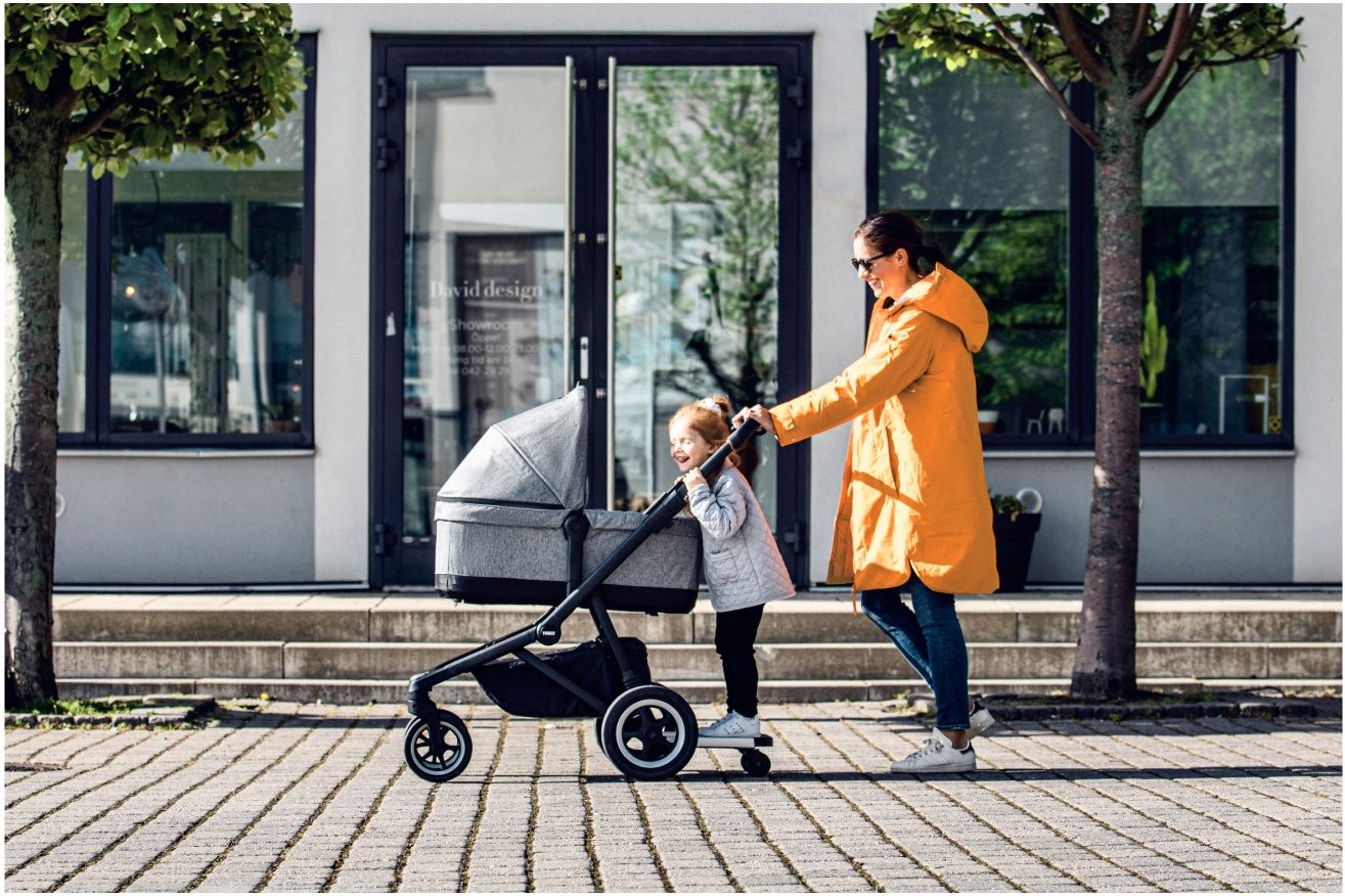 A woman strollers with her child in one of the best full-size strollers at Thule and her toddler on a rider board.
