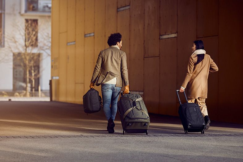Una coppia con cappotto e sciarpa cammina nella città con una valigia Thule.
