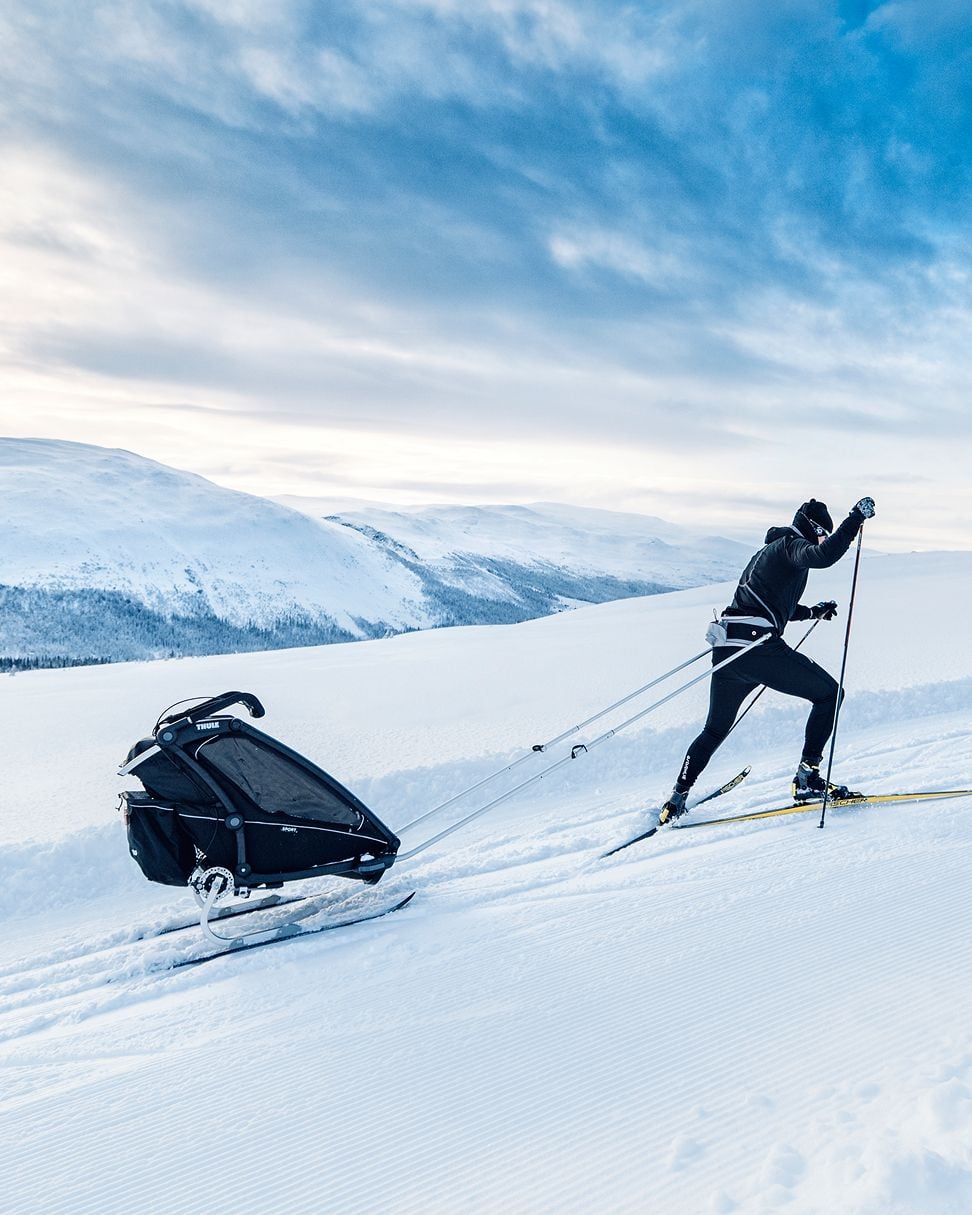 Personne faisant du ski de fond en montée tout en tirant une remorque à vélo.